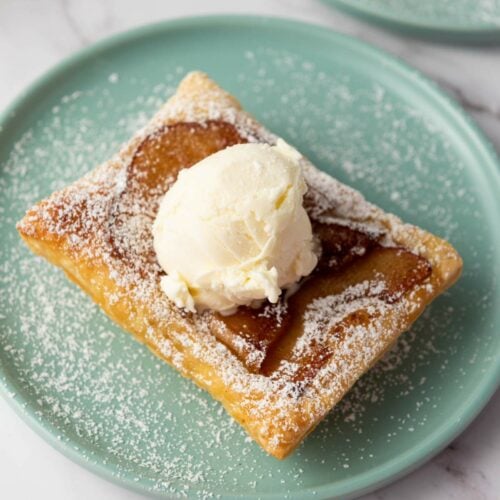 A square puff pastry topped with a scoop of vanilla ice cream and dusted with powdered sugar on a light blue plate.