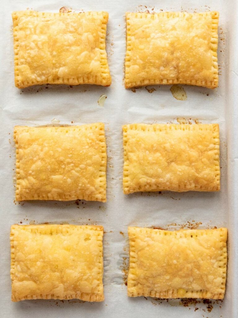 Six rectangular hand pies with golden, flaky crusts are arranged in two rows on a parchment-lined baking sheet.