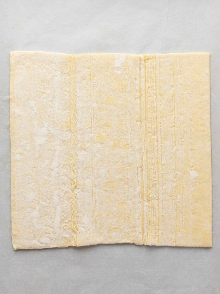A single sheet of uncooked puff pastry dough on a light-colored surface.