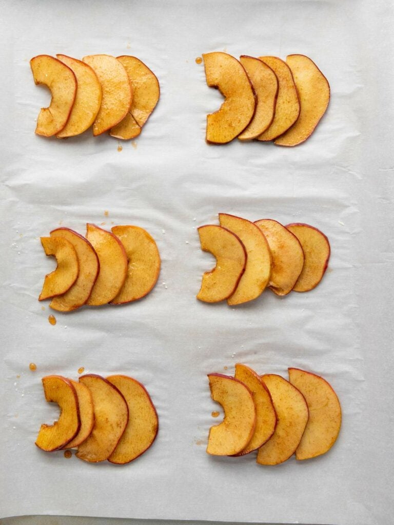 Six groups of thinly sliced apple wedges are arranged on a parchment-lined baking sheet.