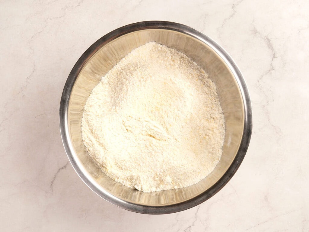 A metal mixing bowl filled with a mound of dry flour on a light-colored marble surface.