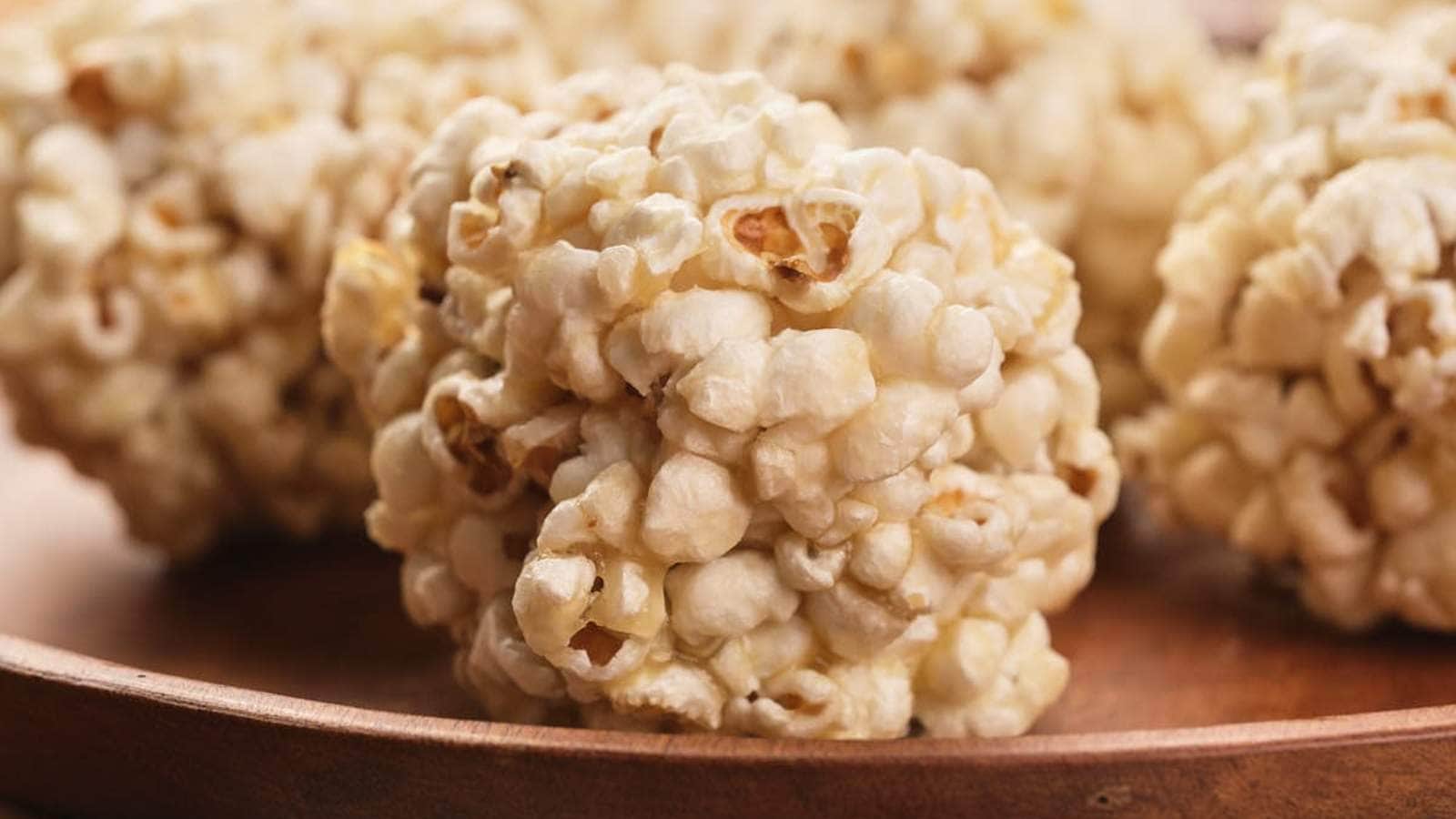 A popcorn ball coated in green sprinkles sits on a blue surface, with candy corn and small candy eyeballs scattered around.