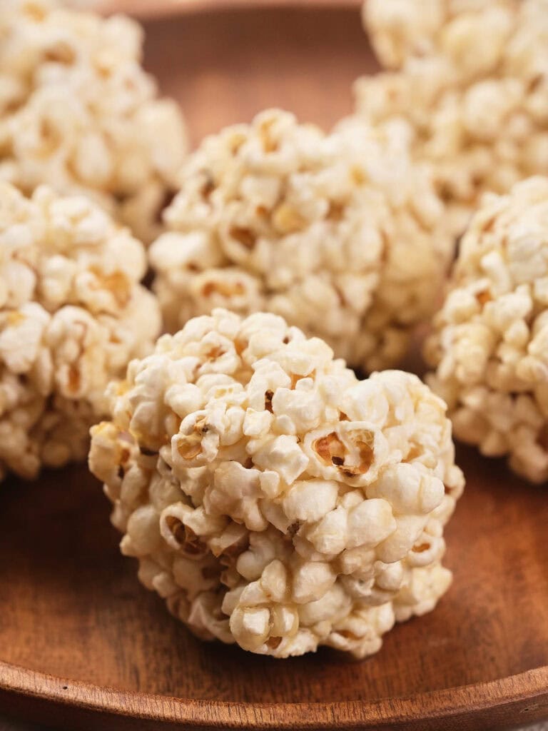 Several popcorn balls are arranged on a wooden plate.