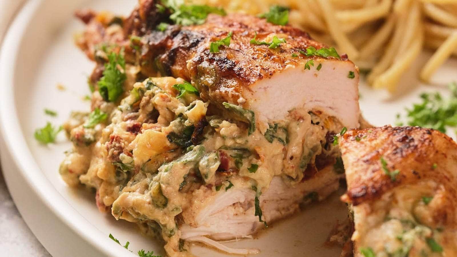 Sliced stuffed chicken breast filled with a creamy mixture of spinach and cheese, garnished with parsley, served with a side of pasta.