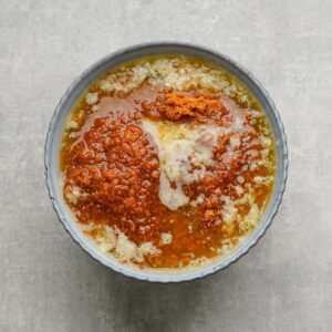 A bowl containing melted butter, brown sugar, and white sugar on a light gray surface.