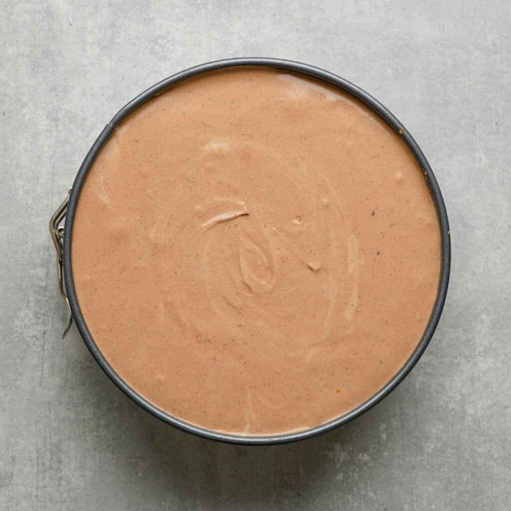 A round pan filled with smooth, light brown batter, viewed from above, on a gray surface.