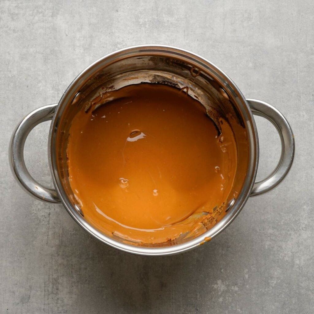 A stainless steel pot filled with smooth, melted brown mixture sits on a gray surface.