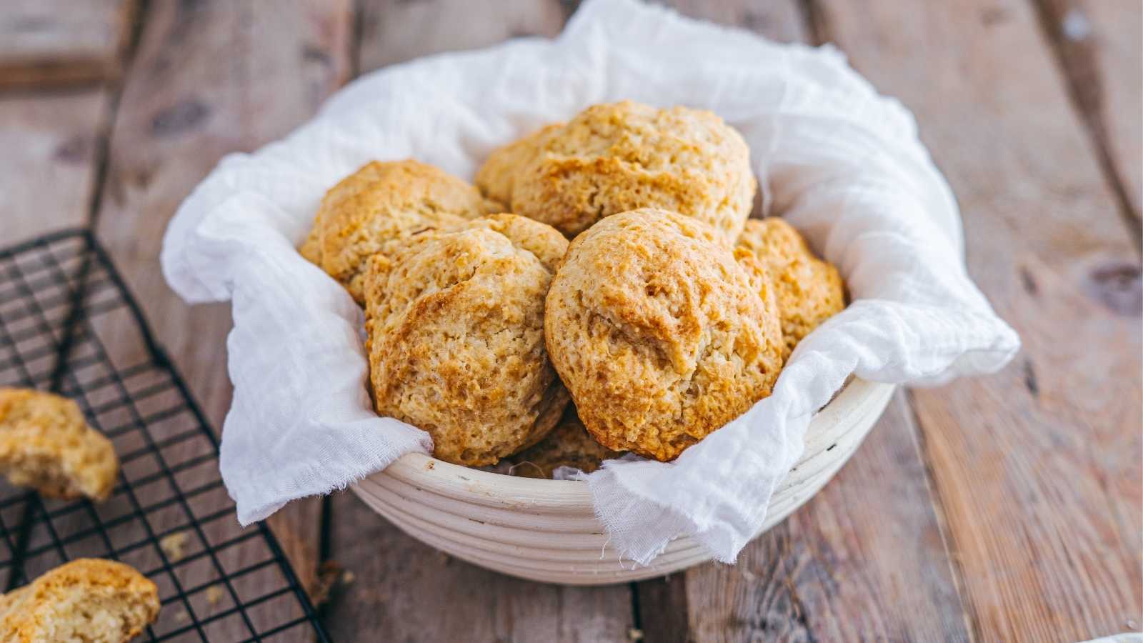 A white bowl lined with a cloth holds several freshly baked buterrmilk biscuits.