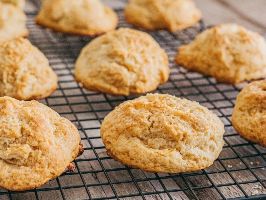 Freshly baked drop biscuits cooling on a black wire rack set on a wooden surface.