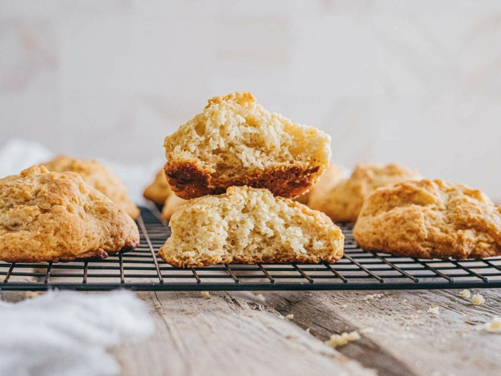Golden brown biscuits sit on a cooling rack, with one biscuit split in half to show its soft, fluffy interior.