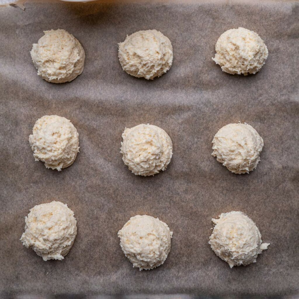 Nine evenly spaced scoops of raw dough on a parchment-lined baking sheet, ready to be baked.
