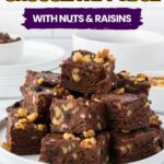 A plate of stacked homemade chocolate fudge pieces with visible nuts and raisins.