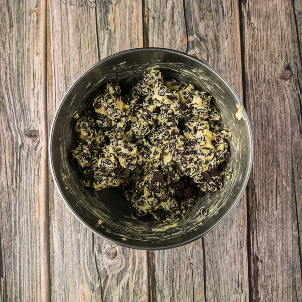 A metal mixing bowl filled with a chocolate mixture sits on a rustic wooden surface.