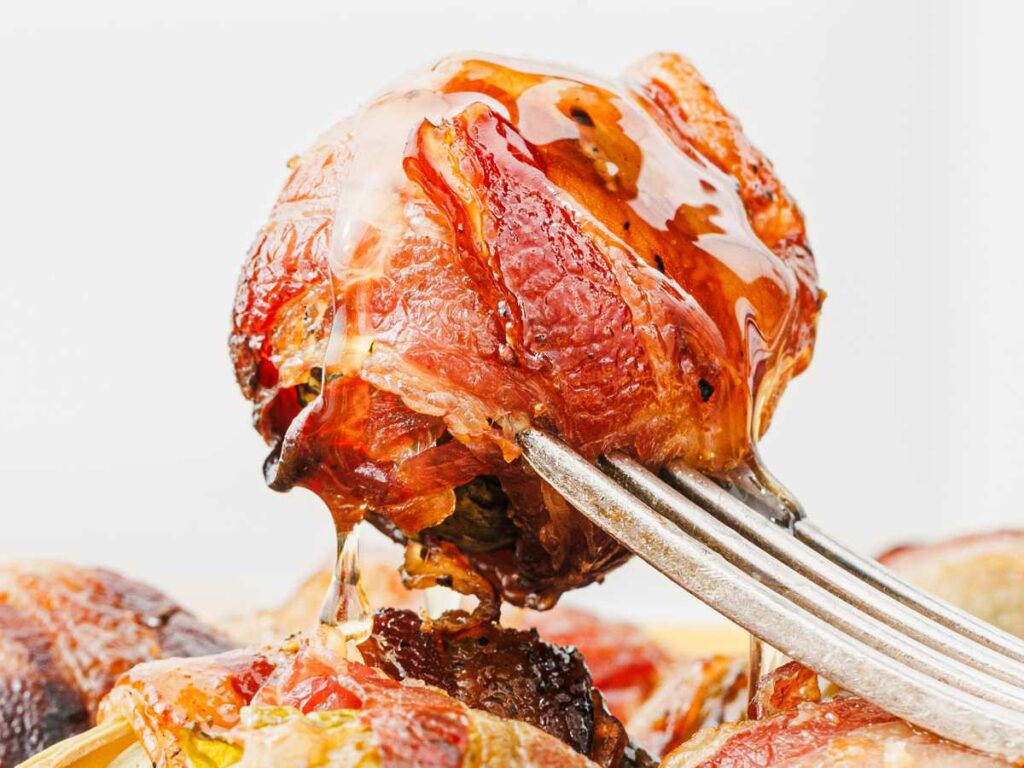 A close-up of a fork holding a piece of roasted meat drizzled with honey or syrup, with more pieces of meat visible in the background.