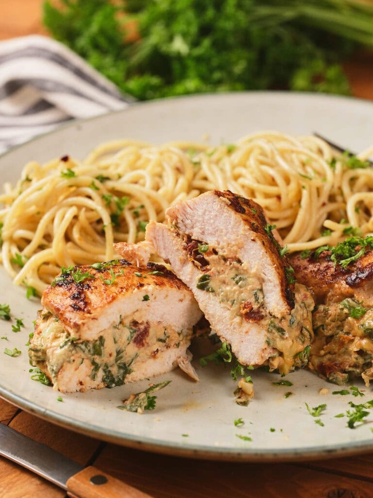 Sliced stuffed chicken breast with a creamy spinach filling, served alongside a portion of plain spaghetti on a plate.