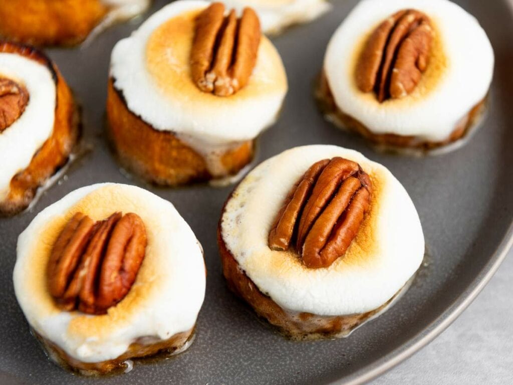 Sliced sweet potatoes topped with toasted marshmallows and pecan halves arranged on a gray plate.