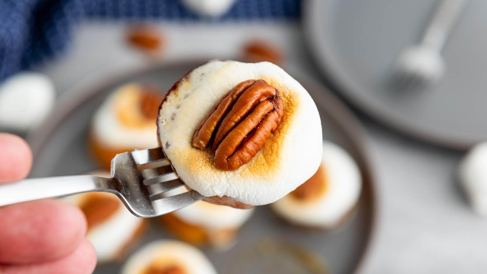 A fork holds a sweet potato appetizer topped with marshmallow and pecan.