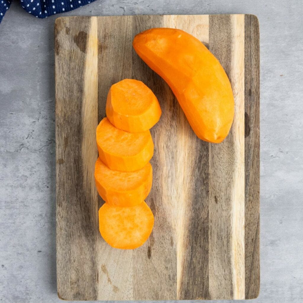 A peeled sweet potato and several round slices arranged on a wooden cutting board.