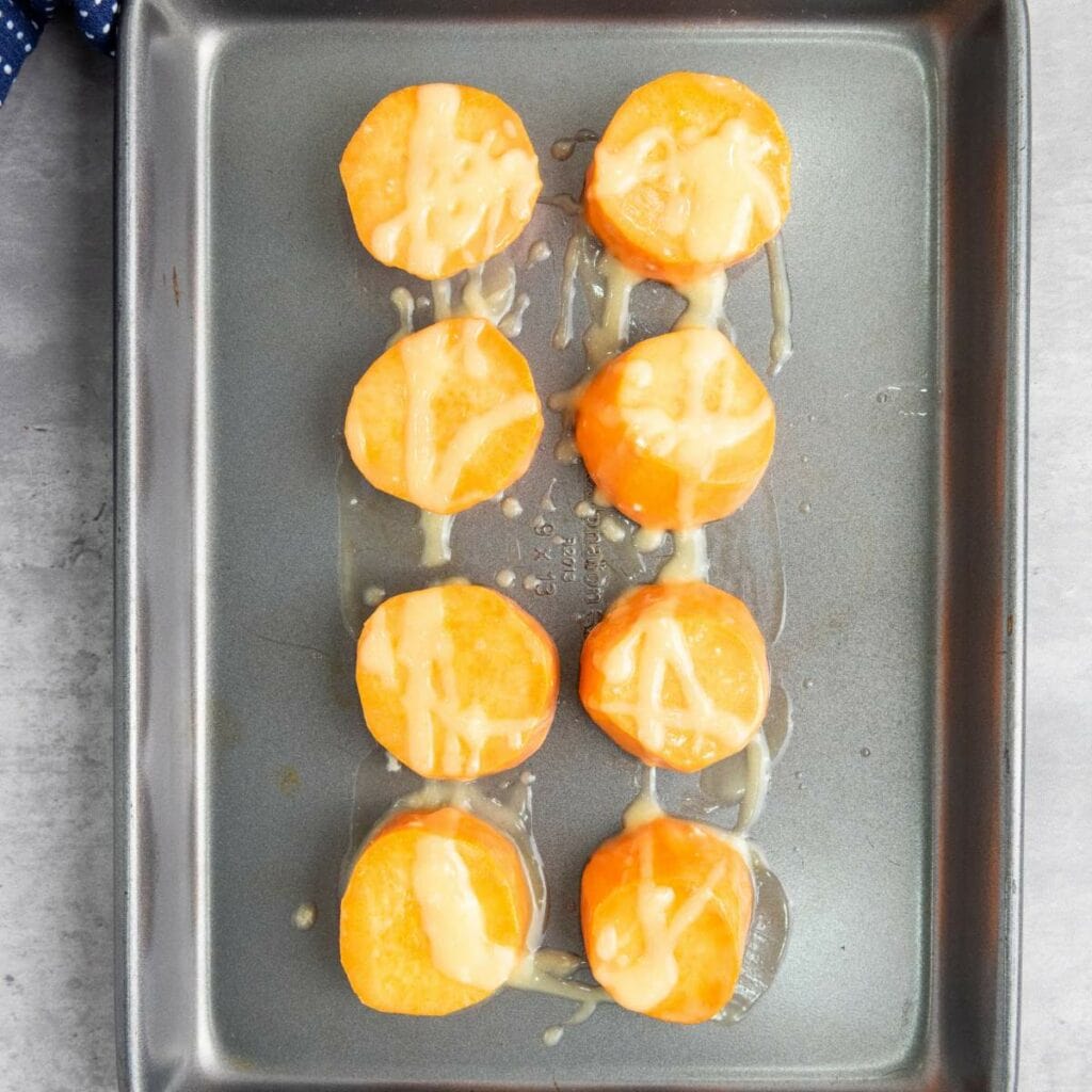 Eight slices of sweet potato topped with a drizzle of syrup arranged in two columns on a baking sheet.