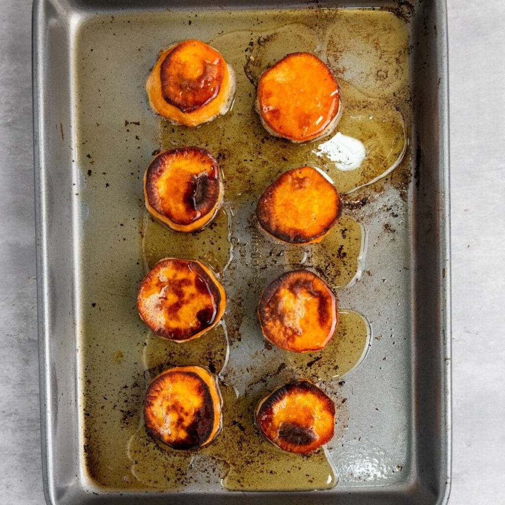 Eight roasted sweet potato slices with caramelized tops are arranged in two columns on a metal baking sheet.