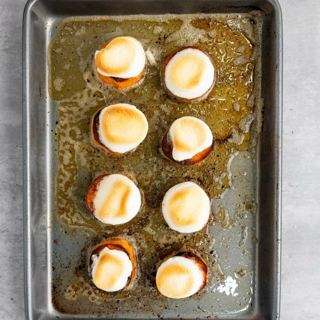 A baking tray with eight sweet potato rounds, each topped with a browned marshmallow.