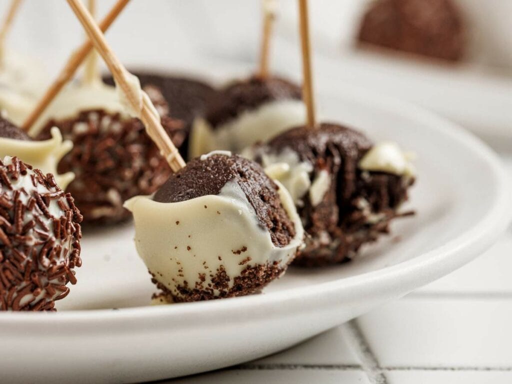 Close-up of chocolate cake pops partially coated in white chocolate, served on a white plate with toothpicks inserted for easy handling.