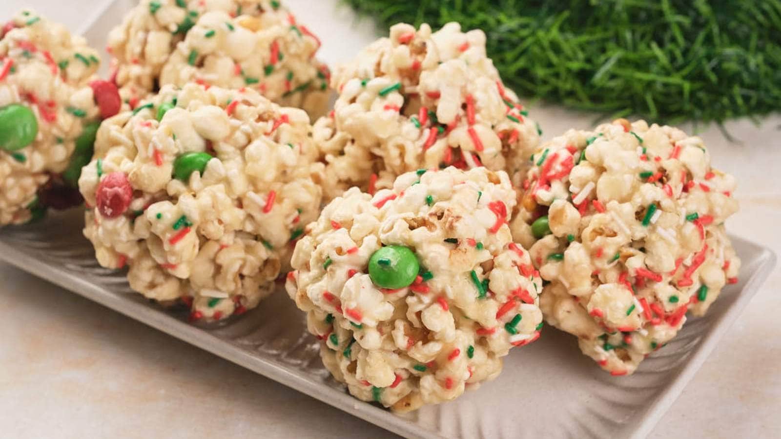 Christmas popcorn balls with colorful red, green, and white sprinkles and candy pieces are arranged on a rectangular white plate.