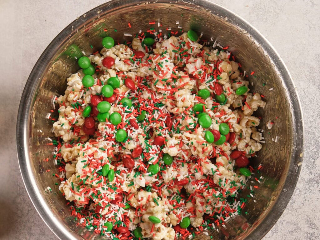 A metal bowl filled with popcorn, red and green candy-coated chocolates, and red, white, and green sprinkles.