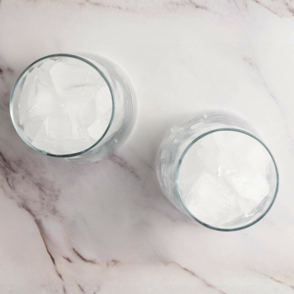 Two clear glasses filled with ice cubes viewed from above on a white marble surface.