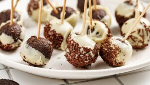 A white plate with Oreo cake pops covered in white chocolate and chocolate sprinkles.