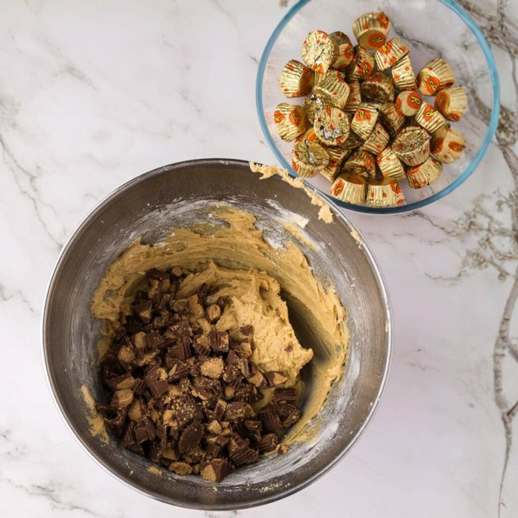 A metal mixing bowl with cookie dough and chopped peanut butter cups.