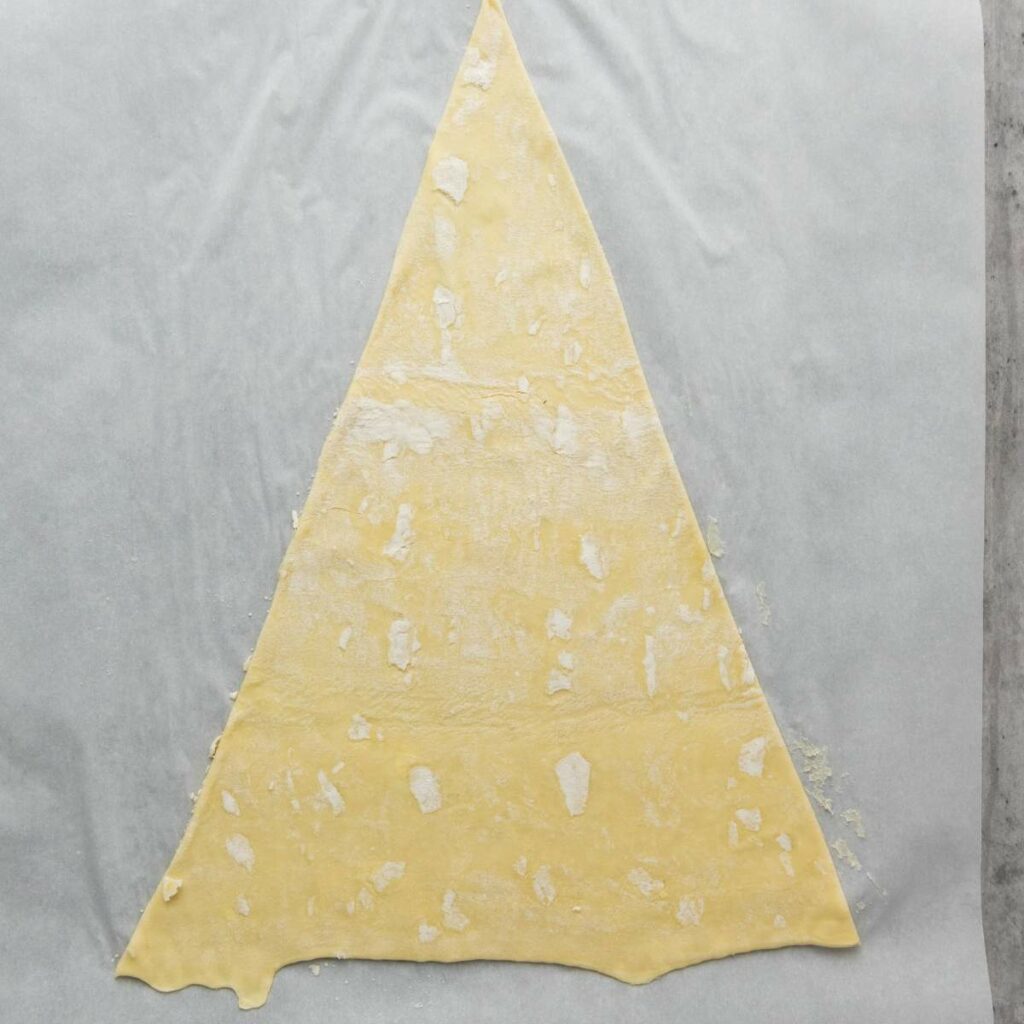 A large, flat triangle of rolled-out dough rests on a sheet of parchment paper.