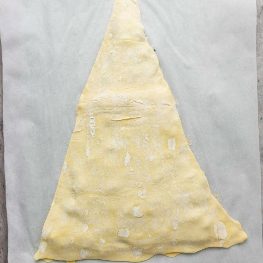 A large triangle of dough is laid flat on a sheet of parchment paper, ready for baking or further preparation.