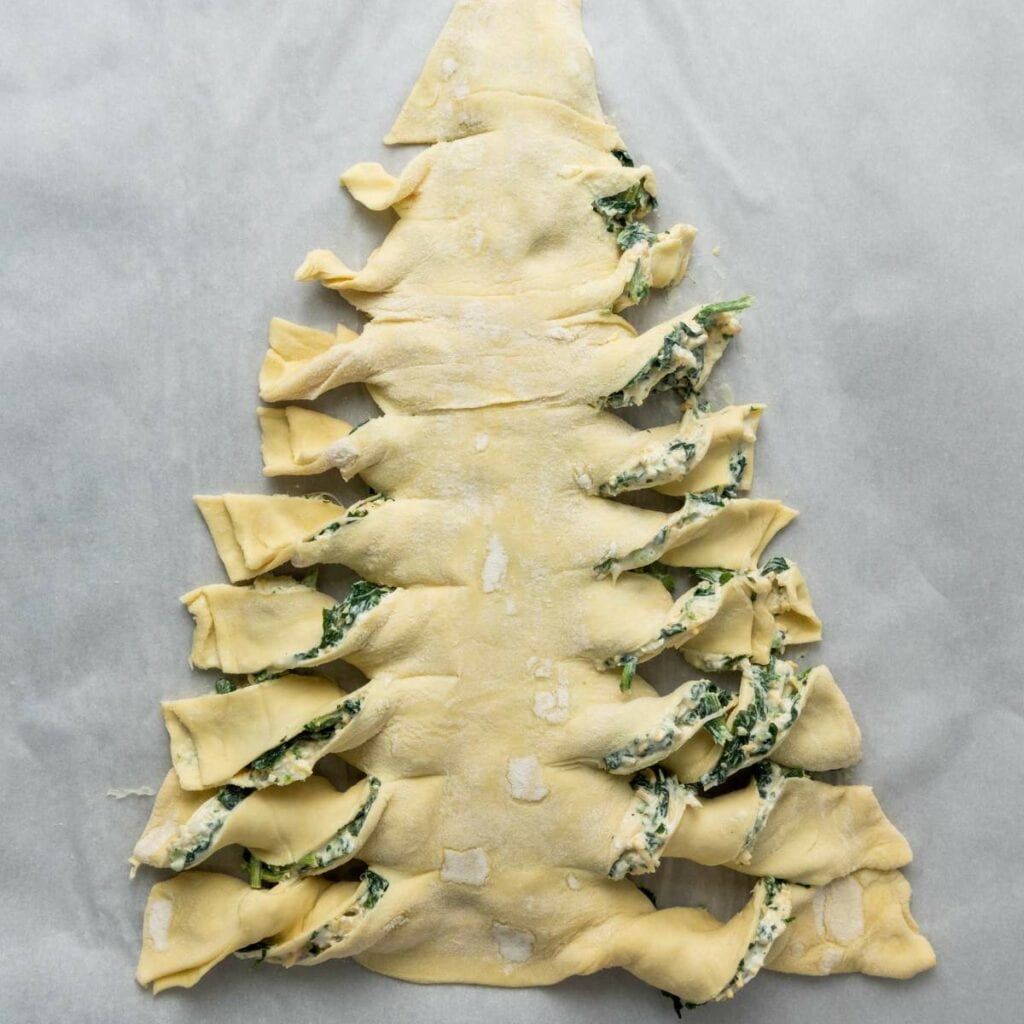 A puff pastry shaped like a Christmas tree, filled with spinach and cheese mixture, is prepared on a sheet of parchment paper.