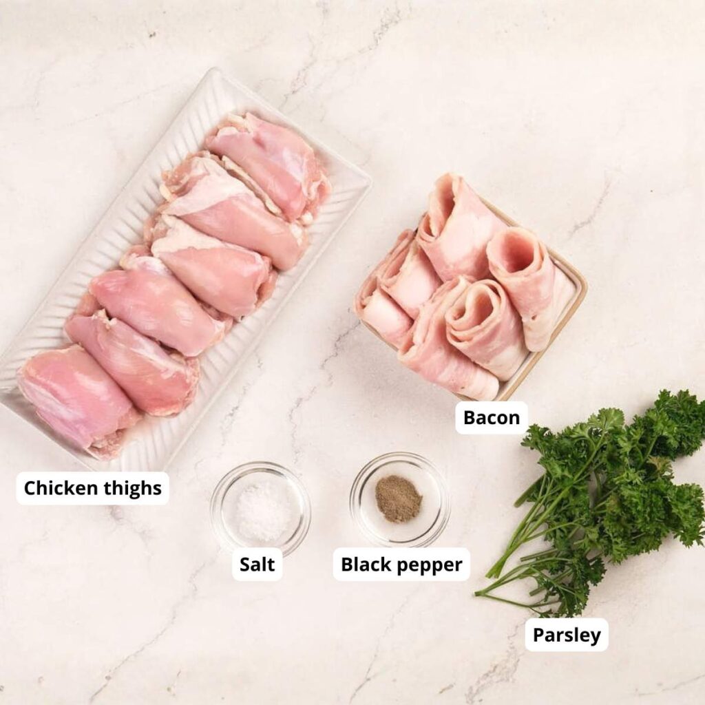 Raw chicken thighs, bacon slices, salt, black pepper, and fresh parsley arranged separately on a white marble surface.