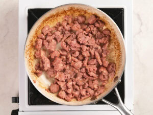 Ground meat is being browned in a stainless steel skillet on a stovetop.