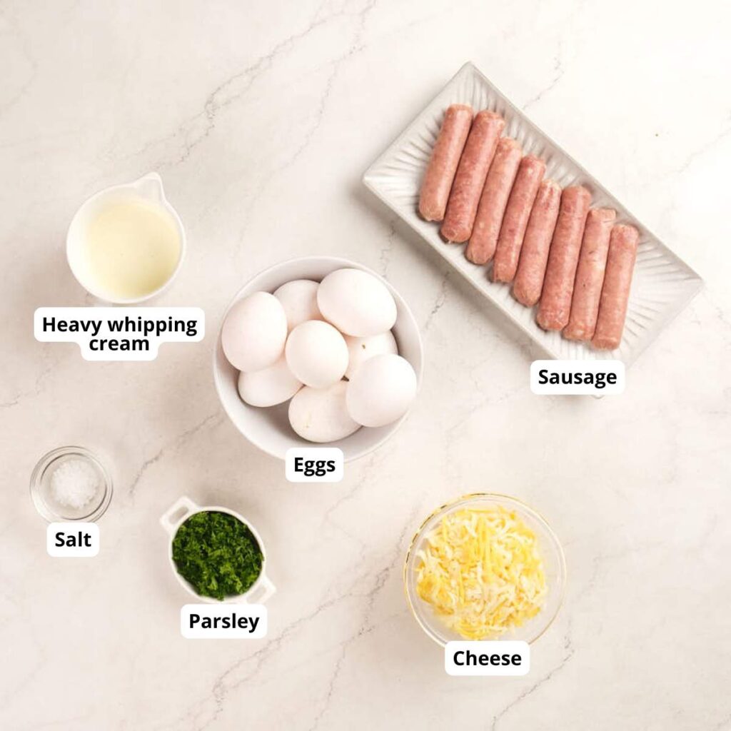 Labeled ingredients on a white surface: heavy whipping cream, sausage links, eggs, salt, chopped parsley, and shredded cheese.