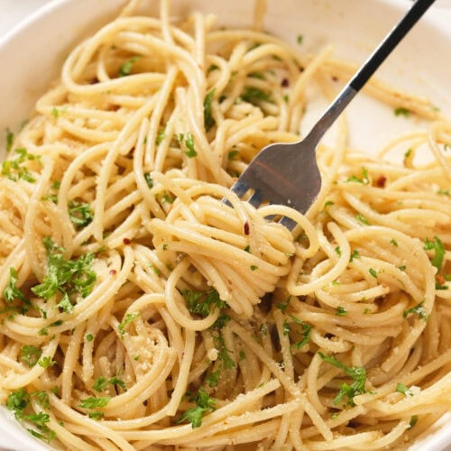 A bowl of spaghetti topped with chopped parsley and grated cheese, with a fork twirling some pasta.