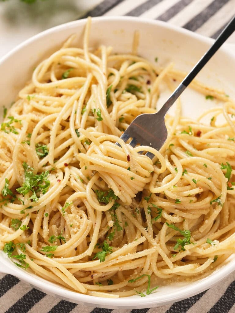 A bowl of spaghetti topped with chopped parsley and grated cheese, with a fork twirling some pasta.