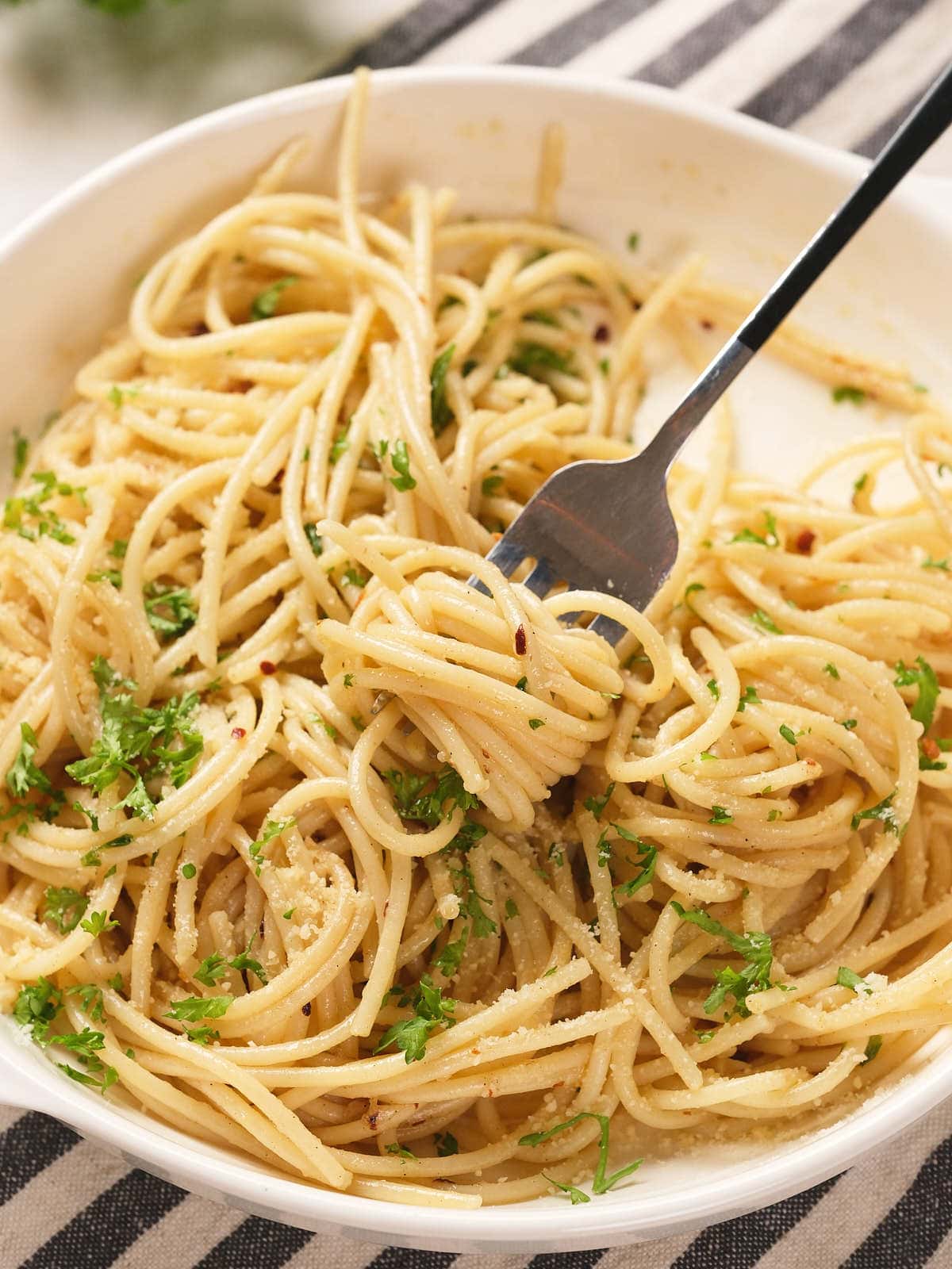 A bowl of spaghetti topped with chopped parsley and grated cheese, with a fork twirling some pasta.