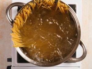 Uncooked spaghetti partially submerged in boiling water in a stainless steel pot on a stovetop.
