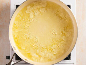 Sliced garlic simmering in melted butter in a pan on a stovetop.