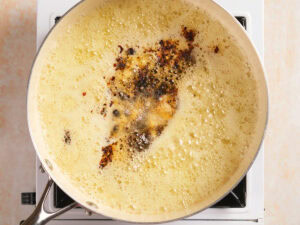 A skillet on a stovetop with bubbling melted butter and brown bits forming in the center.