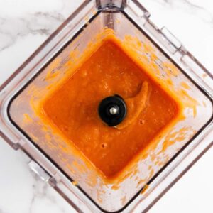 Top view of orange sauce or puree in a blender on a white marble surface.