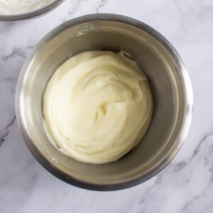 A stainless steel bowl filled with smooth, creamy white mixture on a marble surface.
