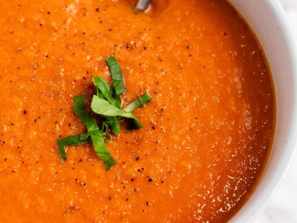 Close-up of a bowl of tomato soup, garnished with chopped fresh basil and black pepper.
